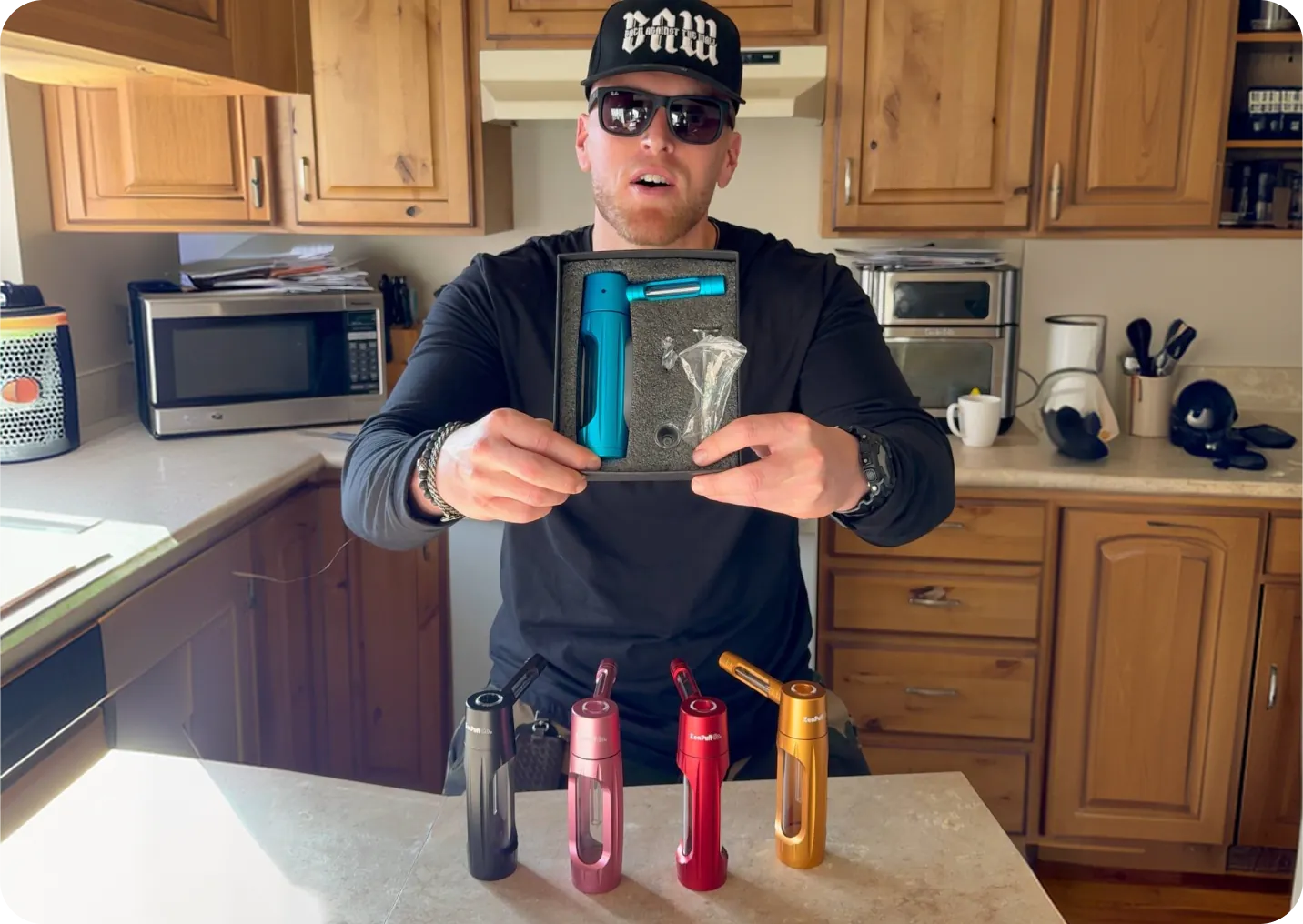 Man in a kitchen holding a teal ZenPuff box above four ZenPuffs